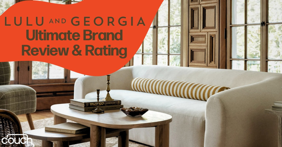 A cozy living room with a white sofa, a striped bolster pillow, and a wooden coffee table with books and a candlestick. Large windows in the background let in natural light. Text overlay reads "Lulu and Georgia Ultimate Brand Review & Rating.