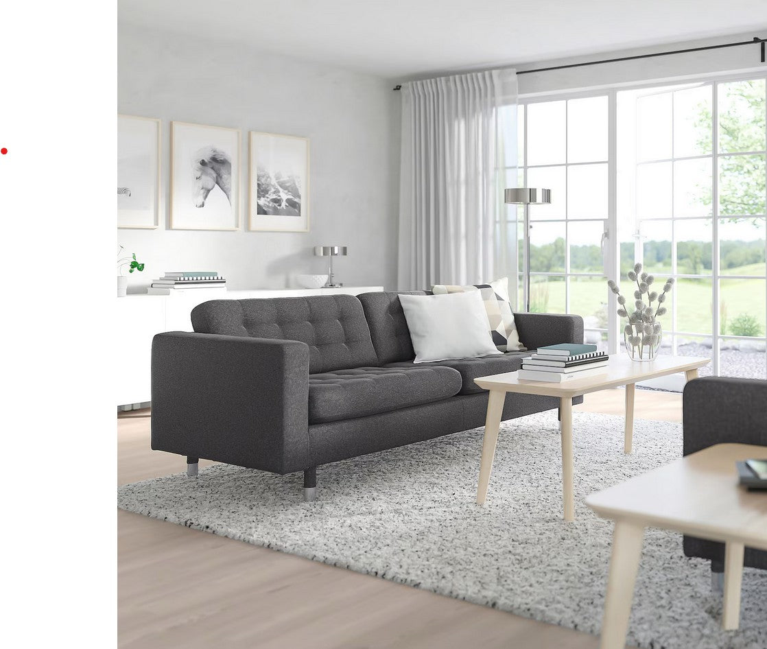 A modern living room featuring the MORABO Sofa in dark gray, complemented by light wooden coffee tables and a plush white rug. Large windows allow natural light to fill the room, while decorative paintings adorn the walls. A floor lamp and curtains add to the serene atmosphere.