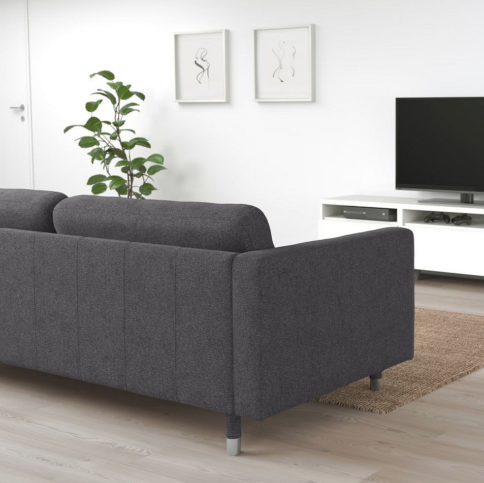 A modern living room featuring the MORABO Sofa in dark gray, a flat-screen TV on a white stand, and two minimalist line drawings on the wall. A green potted plant sits beside the sofa. The room is styled with light wood flooring and a neutral color scheme.