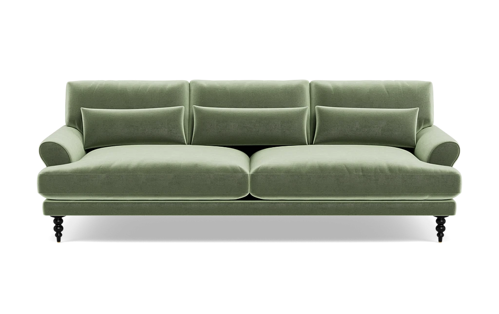 The Maxwell Custom Sofa is a green velvet piece featuring three back cushions, two seat cushions, and a pair of armrests. It comes with four small decorative pillows and rests on four dark wooden legs that give it a classic and elegant appearance.