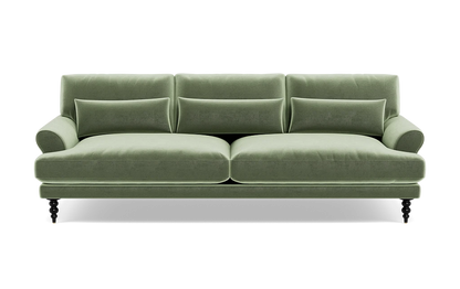 The Maxwell Custom Sofa is a green velvet piece featuring three back cushions, two seat cushions, and a pair of armrests. It comes with four small decorative pillows and rests on four dark wooden legs that give it a classic and elegant appearance.