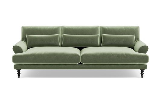 The Maxwell Custom Sofa is a green velvet piece featuring three back cushions, two seat cushions, and a pair of armrests. It comes with four small decorative pillows and rests on four dark wooden legs that give it a classic and elegant appearance.