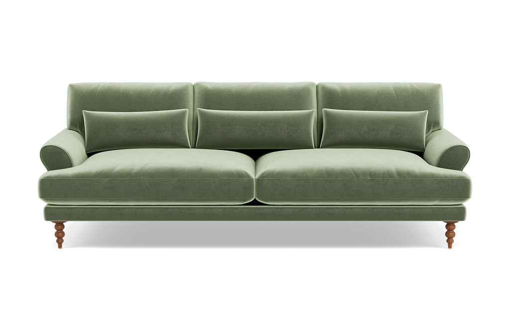 The Maxwell Custom Sofa, upholstered in green velvet, features three seat cushions and matching backrests. It comes with three rectangular pillows and has elegantly rounded armrests. The sofa is supported by four wooden legs, blending a classic touch with its modern design.