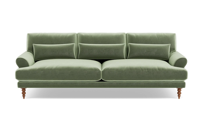 The Maxwell Custom Sofa, upholstered in green velvet, features three seat cushions and matching backrests. It comes with three rectangular pillows and has elegantly rounded armrests. The sofa is supported by four wooden legs, blending a classic touch with its modern design.