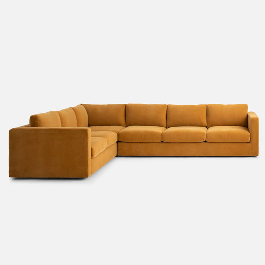 The Milo Sectional is a large, L-shaped sofa in mustard yellow fabric with padded backrests and seating, showcased against a plain white background.