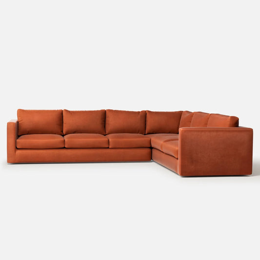 The Milo Sectional is a spacious and contemporary L-shaped sofa upholstered in a burnt orange fabric, featuring plush, cushioned seating and a sleek, minimalist design. It is showcased against a plain white background.