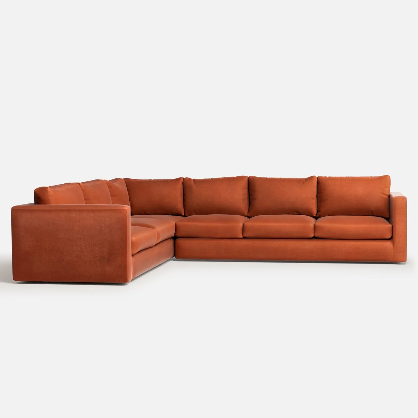 The Milo Sectional is a large, plush L-shaped sofa in a warm rust color, showcased against a plain white background. It features deep cushions and boasts a modern, boxy design.