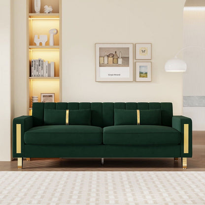 A modern living room with a Mid Century Modern Sofa Couch in dark green velvet, highlighted by elegant gold accents. The sofa is set against a cream-colored wall adorned with two framed pictures above it. To the left, there is a built-in shelf filled with books and decor, while on the right, a white pendant light hangs gracefully.