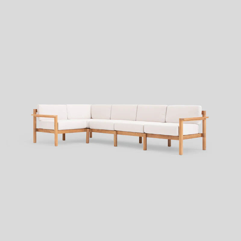 A neutral-colored L-shaped sofa with a light wood frame and off-white cushions is set against a plain gray background. The design is minimalistic, featuring clean lines and a contemporary style.