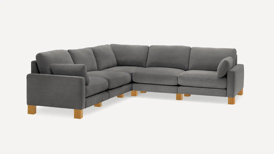 The Union Fabric Modular 5-Seat Sofa Sectional, featuring a large L-shaped design in gray with thick cushions and wooden legs, is set against a plain white background. This sofa boasts a modern aesthetic and a plush appearance, offering ample seating space.