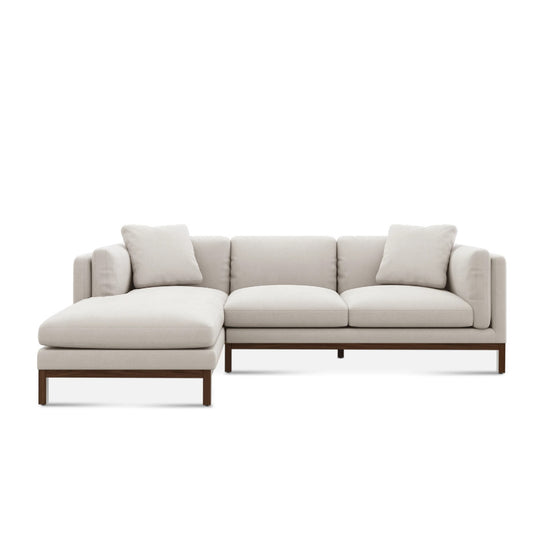 The Owen Chaise Sectional Sofa is a contemporary beige piece featuring a wooden base and clean lines, complete with a chaise on the left and minimalist cushions for enhanced comfort and modern style.