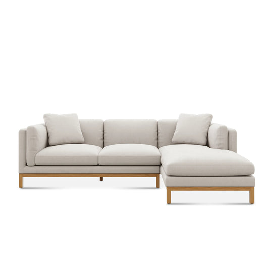 The Owen Chaise Sectional Sofa is a contemporary piece featuring light beige upholstery and stylish wooden accents. It boasts a right-side chaise lounge and is displayed against a simple white background.