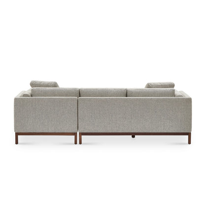 The image depicts the back view of the Owen Chaise Sectional Sofa, showcasing its modern light gray upholstery complemented by wooden legs. The design is characterized by clean lines and a minimalist aesthetic that contribute to its sleek, contemporary look.