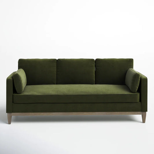 The Pera 84" Upholstered Sofa is a modern piece in dark green velvet, featuring three back cushions and two side pillows. It showcases a sleek design with wooden legs, all set against a plain white background.