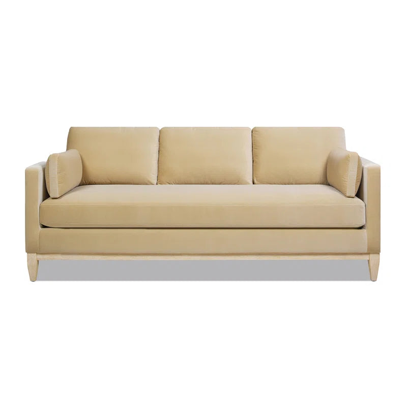 The Pera 84" Upholstered Sofa is a beige, modern three-seater with clean lines and a minimalist design. It includes two rectangular arm cushions and a cushioned backrest, all set against a white background.