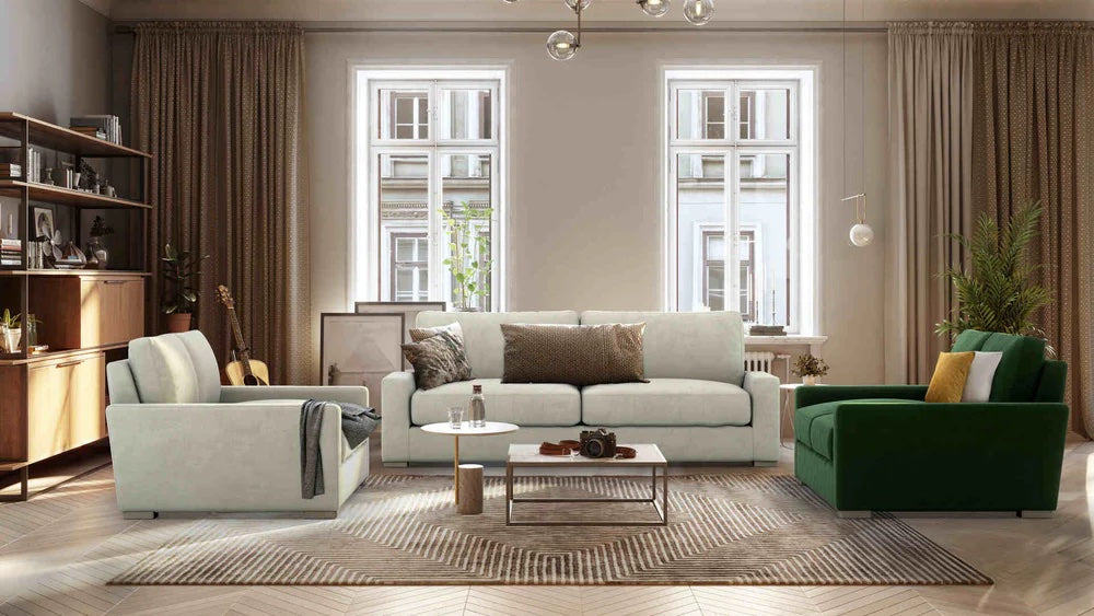 A modern living room with a beige 3-seater sofa, a green armchair, and a light armchair around a wooden coffee table. Large windows with beige curtains allow natural light in, illuminating the room's wooden flooring, bookshelves, a guitar, and plant decor.