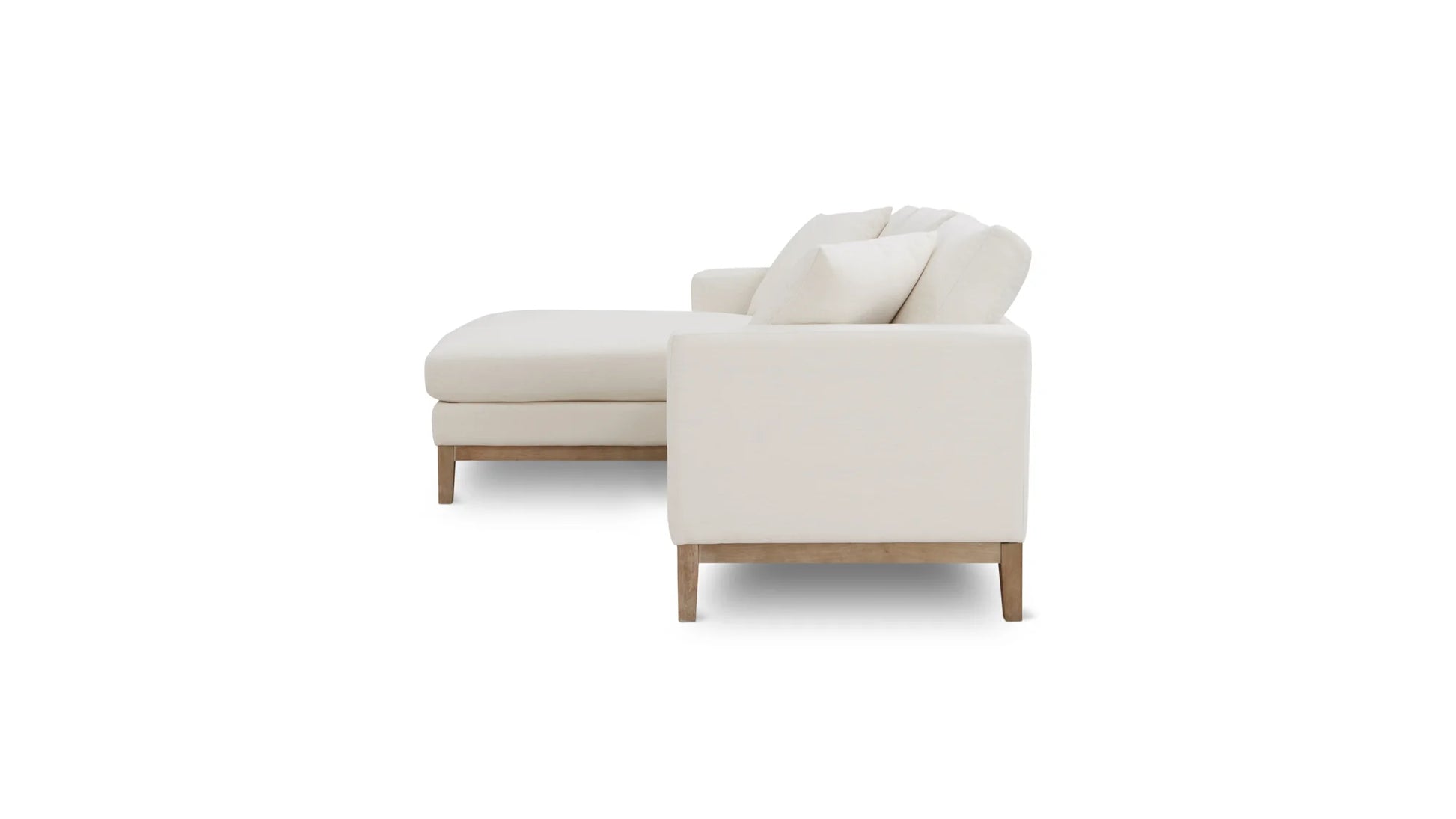 The Any Day Sectional is shown in a side view, highlighting its modern white design with a chaise lounge extension. It boasts plush cushions and rests on wooden legs, set against a plain white background.