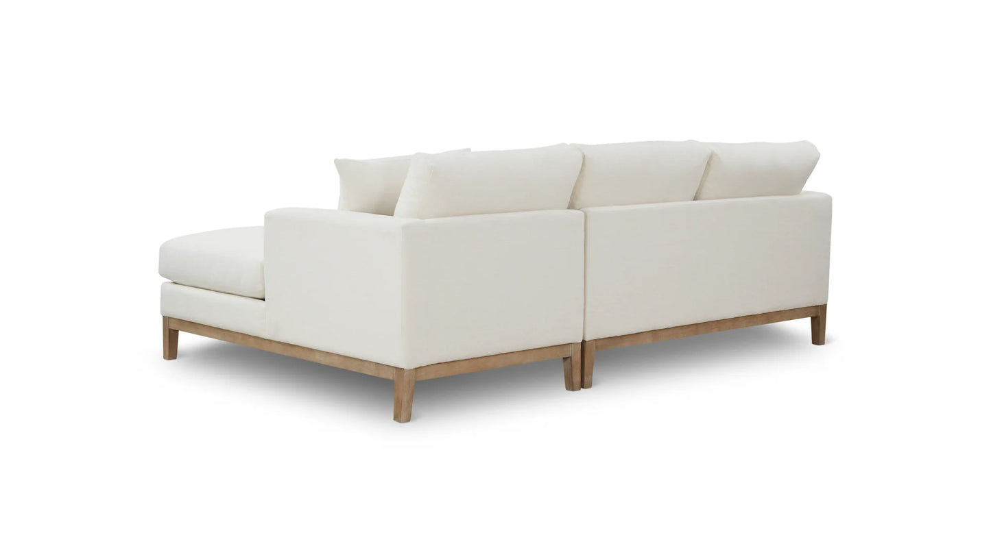 The Any Day Sectional is a white sofa with a modern design, featuring plush cushions and a wooden base. It is showcased on a plain white background to accentuate its clean lines and contemporary style.