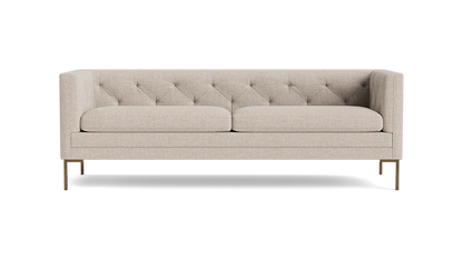 The Sit Tight 90" Sofa, featuring a beige tufted design with two cushions, is showcased against a solid black backdrop. Its minimalist aesthetic and wooden legs blend elegance with simplicity.