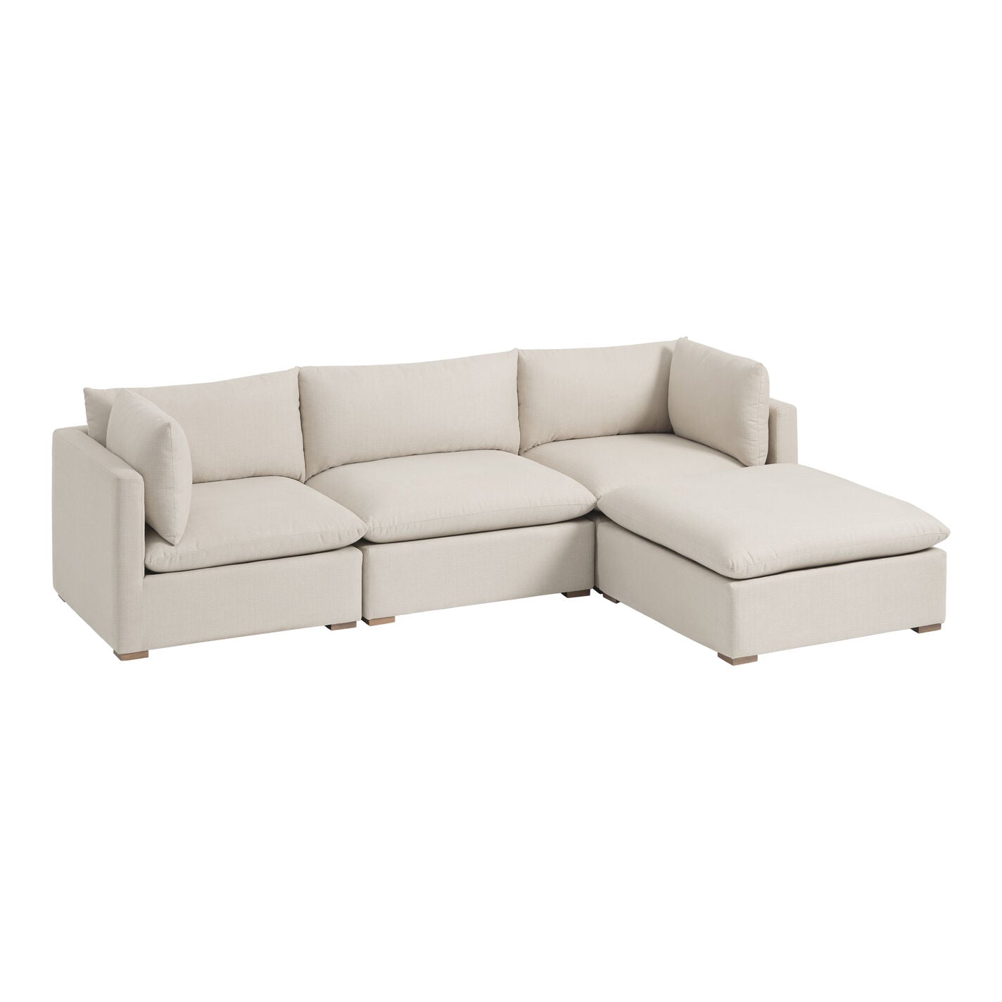 The Weston Sand Pillow Top 4-Piece L Modular Sectional Sofa is a beige L-shaped couch featuring three cushioned seats, a right-side chaise lounge, and two matching pillow armrests. It boasts a minimalist design with wooden block feet, all set against a white background.