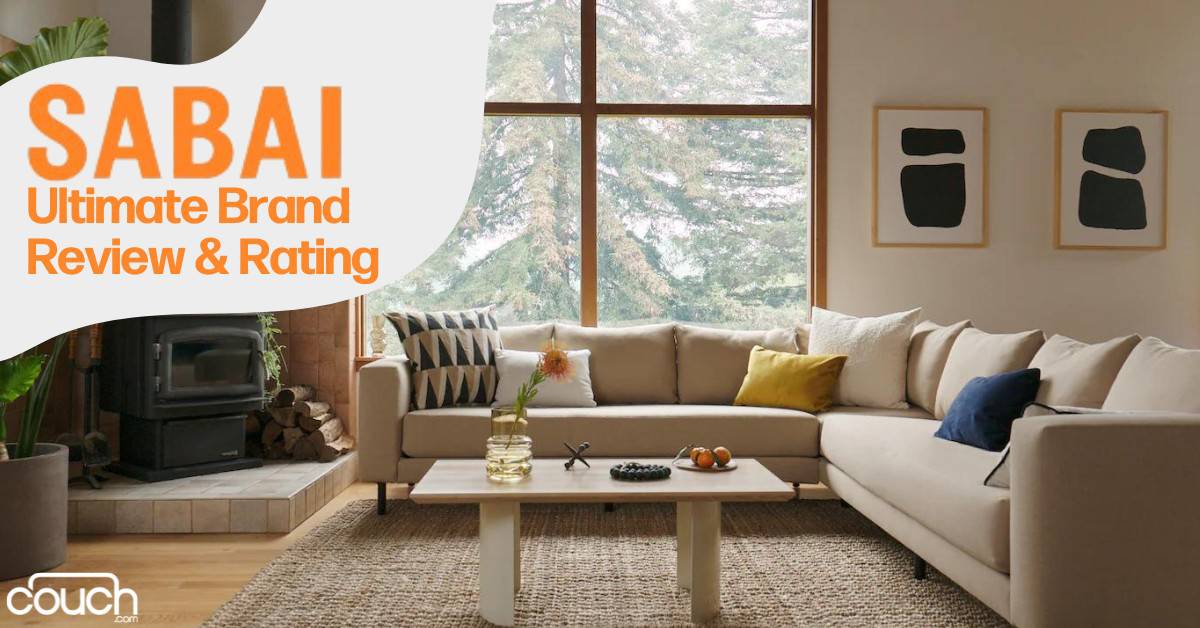 A cozy living room with a large L-shaped beige sofa adorned with various throw pillows, a wooden coffee table with decorative items, and a modern wood-burning stove. The room features large windows with a snowy forest view. Text overlay reads "SABAI Ultimate Brand Review & Rating".