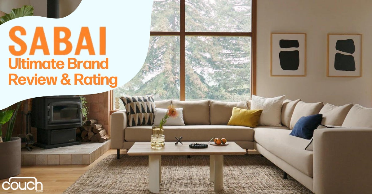 A cozy living room with a large beige sectional sofa, colorful cushions, and a wooden coffee table. A fireplace is in the corner, and large windows showcase a snowy landscape outside. Text reads "Sabai Ultimate Brand Review & Rating".