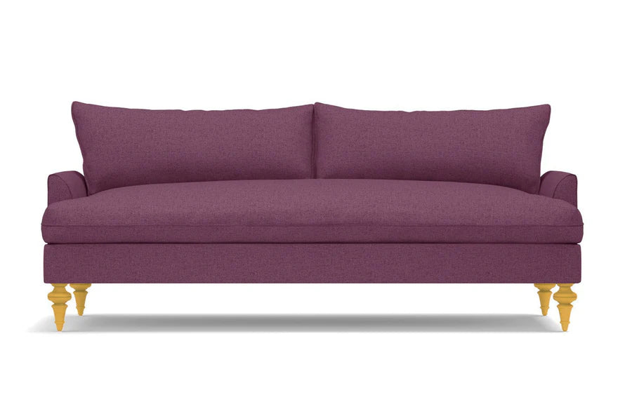 The Saxon Sofa is a sleek design in a plum color, featuring two back cushions and wooden legs. Its smooth, modern upholstery adds a touch of elegance to any room.