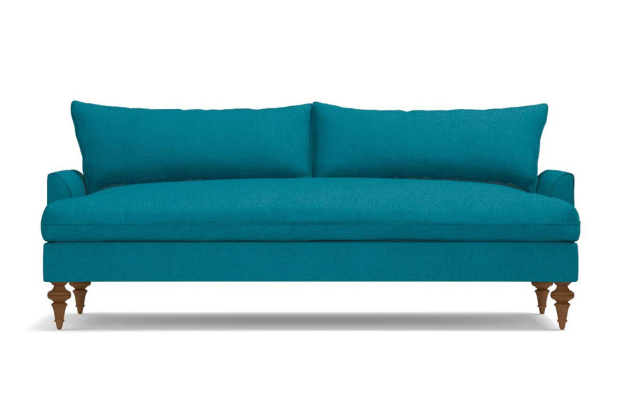 Introducing the Saxon Sofa, a modern piece with a minimalist design in teal. This elegant sofa features two seat cushions and wooden legs, with a low back and clean lines that bring a contemporary touch to any room. It is beautifully showcased against a plain white background.