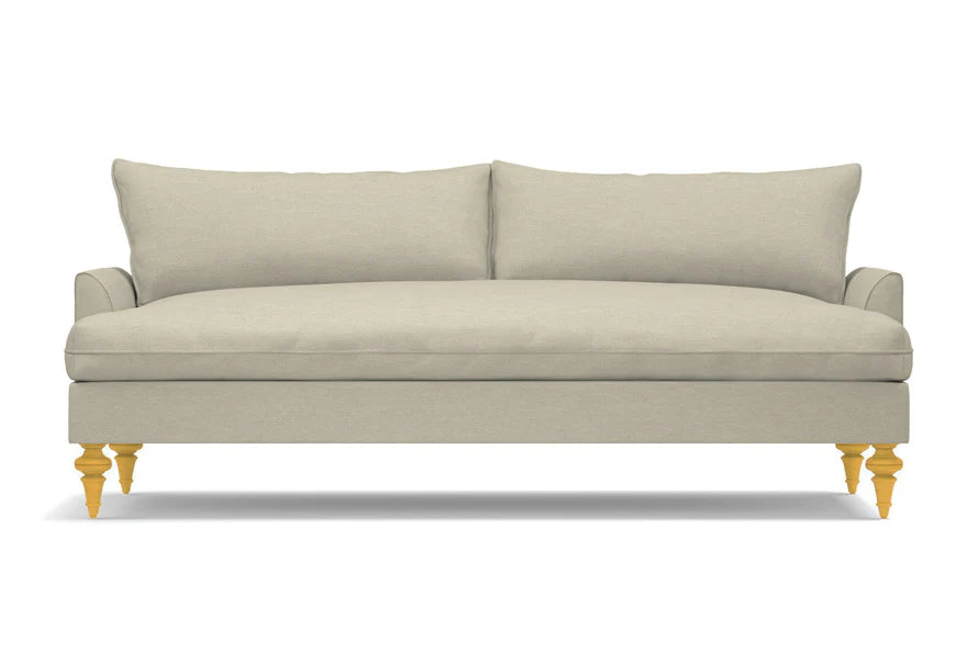 A Saxon Sofa in beige, featuring two large cushions and wooden legs, set against a white background. Its minimalist and modern design provides a clean and sophisticated appearance.