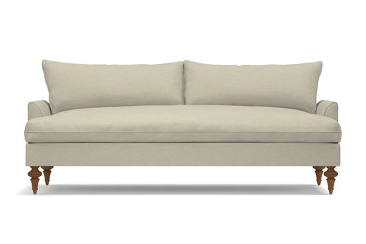 The Saxon Sofa is a minimalist, beige three-seater featuring two large back cushions and wooden legs. It rests on a white background and boasts a plush, cushioned seating area.