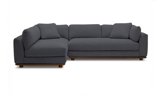 The Miller Sectional is a contemporary L-shaped sofa featuring dark gray upholstery and wooden legs, showcased against a plain white background.