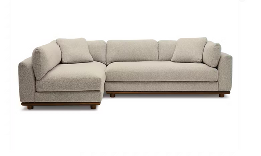 The Miller Sectional is a light beige L-shaped sofa with a textured fabric finish, featuring plush cushions and dark wooden legs, set against a plain white background.