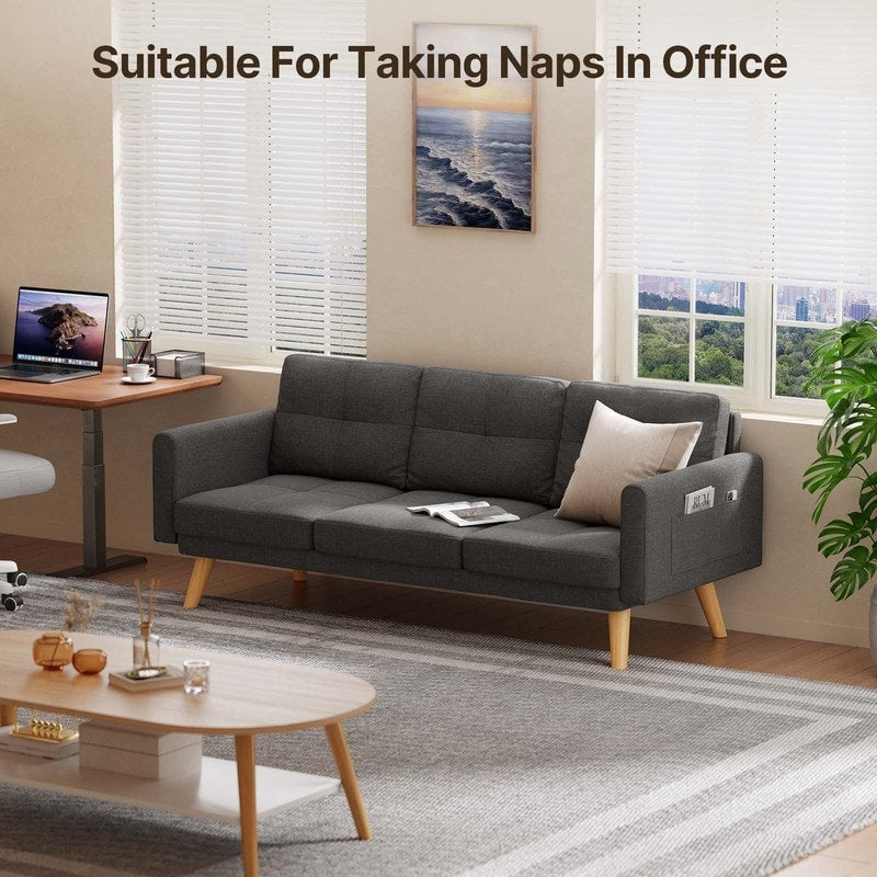 A cozy office space with a dark gray Sofa Couch Small Loveseat, complete with 3 comfy pillows for added comfort, is ideal for taking naps. The room features large windows, a desk with a computer, and a coffee table adorned with decor.