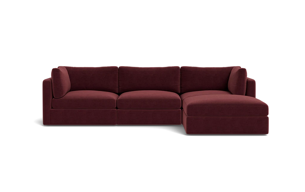 The Tatum Modular 3 Seat Chaise 106" Sectional, with its maroon upholstery and plush cushions, is showcased against a solid black backdrop. This stylish design includes three connected seats and a chaise lounge positioned on the right side.