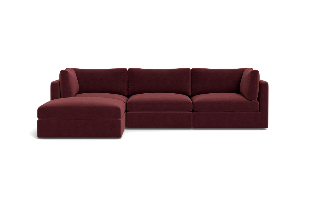 The Tatum Modular 3 Seat Chaise Sectional, upholstered in maroon, sits against a solid black background. It boasts plush cushions and a chaise lounge on the left side, providing a modern and comfortable seating option.