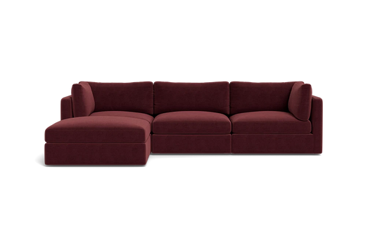 The Tatum Modular 3 Seat Chaise Sectional, upholstered in maroon, sits against a solid black background. It boasts plush cushions and a chaise lounge on the left side, providing a modern and comfortable seating option.