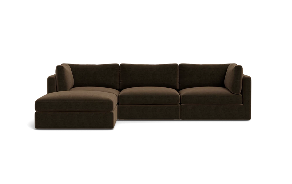 The Tatum Modular 3 Seat Chaise Sectional, featuring a large, dark brown design with cushioned seats and backrests, is displayed against a solid black background. It includes a chaise lounge on the left side, offering ample seating space.