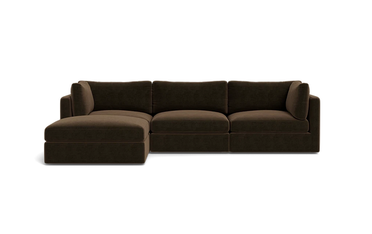 The Tatum Modular 3 Seat Chaise Sectional, featuring a large, dark brown design with cushioned seats and backrests, is displayed against a solid black background. It includes a chaise lounge on the left side, offering ample seating space.