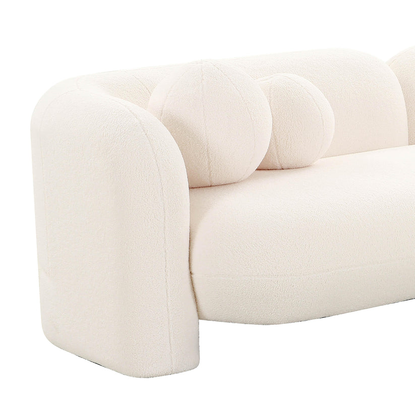 The Amelie Faux Fur Sofa is a plush, cream-colored piece featuring a curved back and armrest. It includes two round, cushion-like accents on the seat for a unique and modern design touch.