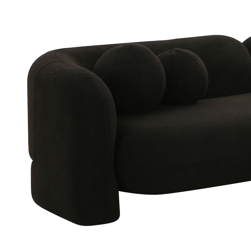 The Amelie Faux Fur Sofa boasts a minimalist design with its black finish, characterized by rounded edges and two spherical cushions, offering a sleek, contemporary look.