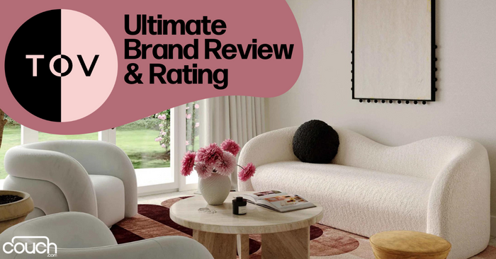 A modern living room with a white curved sofa, round wooden tables, and pink flowers in a vase. Large windows showcase a garden. Text on a pink background reads "Ultimate Brand Review & Rating" with the logo "TOV" and "couch.com" at the bottom.