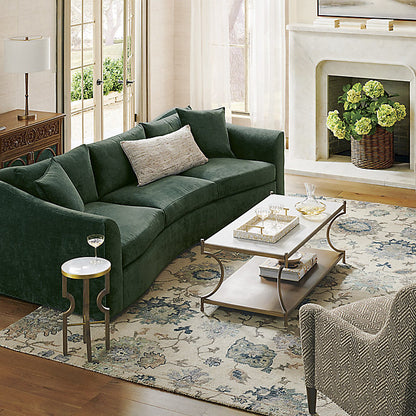 Living room featuring the Pippa Sofa in green, accompanied by a patterned armchair and a floral rug. A two-tiered coffee table displays decorative items and glassware, while the fireplace showcases a vase of green hydrangeas beside a window with sheer curtains.