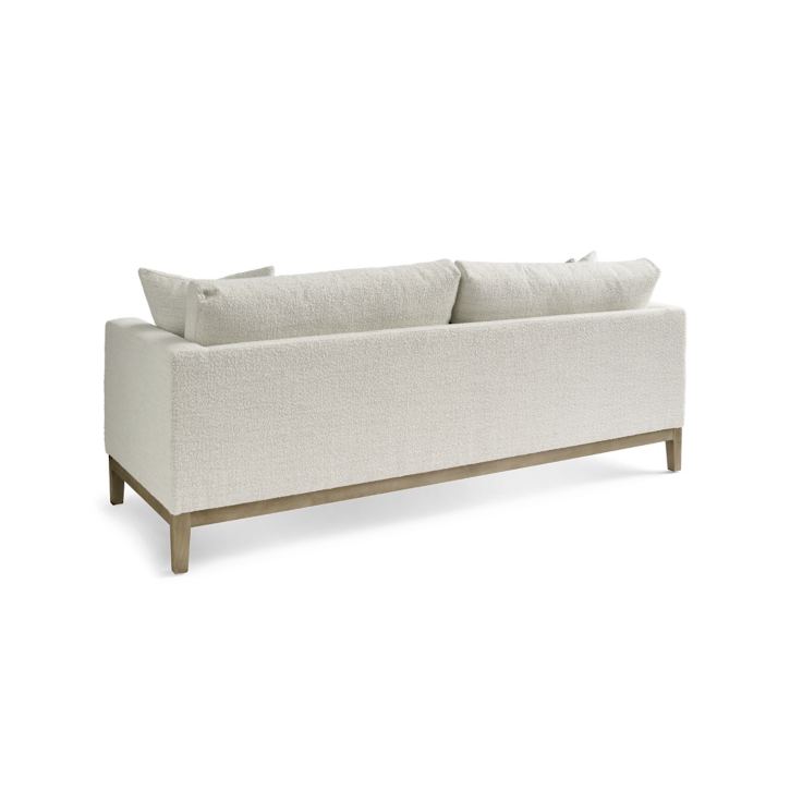 The Capri Sofa, featuring a light gray, modern design with wooden legs and two large back cushions, is depicted from the back against a plain white background.