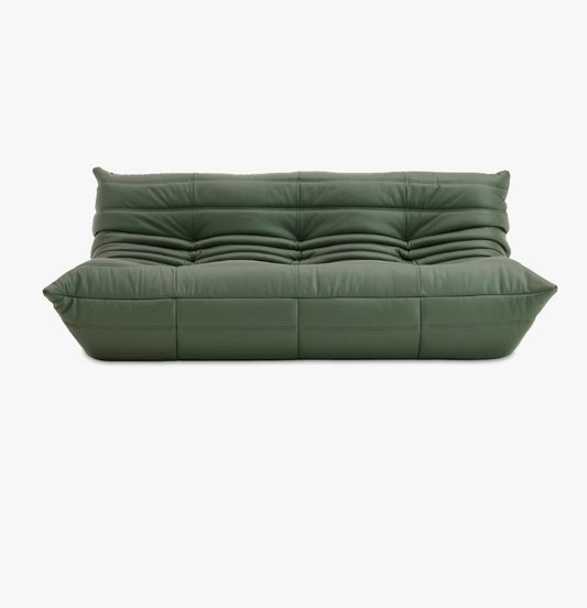 The Togo Sofa in Opera Leather boasts a modern, plush design with a green tufted finish against a clean white background. It features a low profile with distinct stitching and padding, offering a contemporary look.