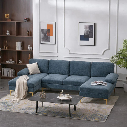 A contemporary living room featuring an elegant U Shaped 4 Seat Indoor Modular Sofa in blue, complemented by a beige throw and cushion. The space includes a sleek black rectangular coffee table, shelves lined with books, two abstract paintings adorning the walls, and a potted plant adding a touch of greenery in the corner.