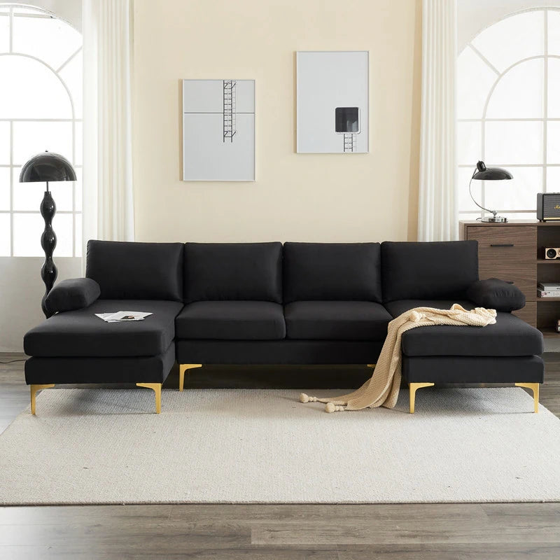 A modern living room boasts an elegant U Shaped 4 Seat Indoor Modular Sofa in sleek black, highlighted by eye-catching gold legs. A beige throw adds a touch of coziness to the sofa. The space is enhanced by large windows, a light-colored rug, abstract wall art, two floor lamps, and a wooden cabinet.