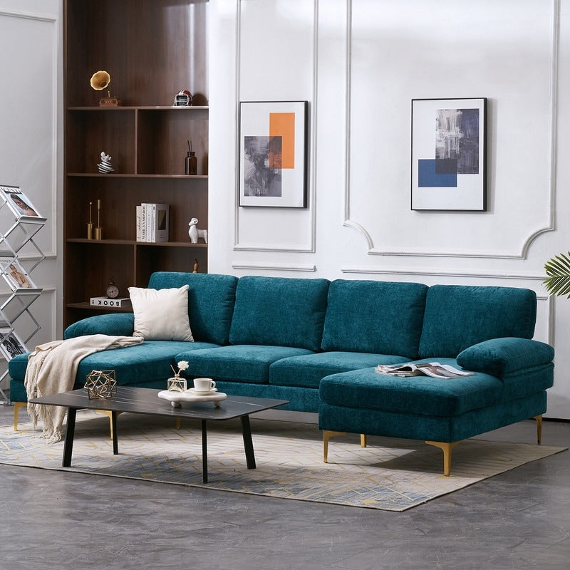 A modern living room showcases a U Shaped 4 Seat Indoor Modular Sofa in teal, accompanied by a dark wood coffee table adorned with decorative items and complemented by a patterned rug. Abstract art graces the white paneled wall, while a large bookshelf occupies the corner.