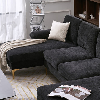 A contemporary living room featuring a dark gray U-Shaped 4 Seat Indoor Modular Sofa, accented by a white pillow and a light throw blanket. On the floor, there's a geometric-patterned rug. In the background, you'll find a magazine rack and a wooden shelf adorned with decorative items.