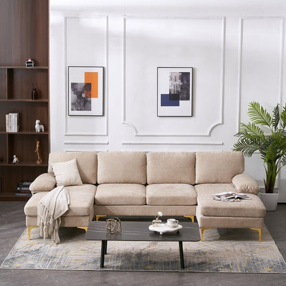 A U Shaped 4 Seat Indoor Modular Sofa in beige, adorned with cushions and a throw blanket, is arranged in a modern living room. In front of it sits a black coffee table decorated with various items. Two abstract paintings are displayed on the white wall, and a potted plant is positioned next to a wooden bookshelf.