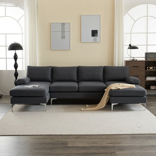 A modern living room showcases a dark gray U Shaped 4 Seat Indoor Modular Sofa with a beige throw blanket draped over one end. The room includes a light beige rug, two framed artworks on the wall, a black floor lamp, and a desk with both a lamp and chair.